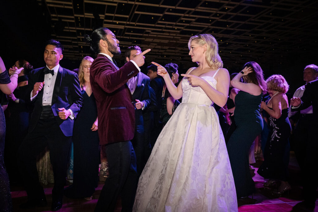 The bride and groom dance and point at each other in the middle of a packed dance floor, their families and friends around them, at a Tokyo wedding.