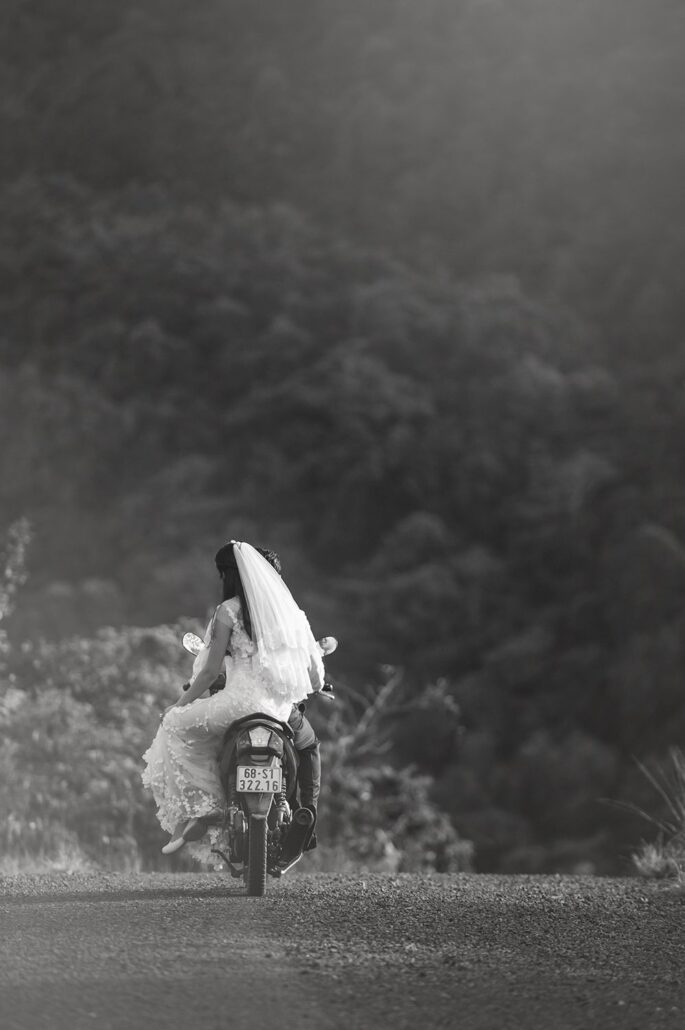 In black and white, the bride rides off on a motorbike along a country road in Vietnam, her veil flying behind her.