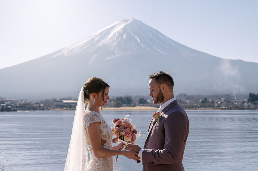 The bride faces the groom by Lake Kawaguchi with Mt Fuji white and close behind, a December elopement in Fuji's clearest season.