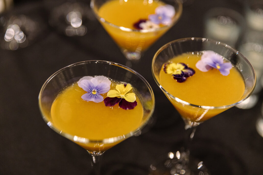 Golden cocktails crowned with edible violas wait on a dark table at a ryokan wedding reception at Jinya.