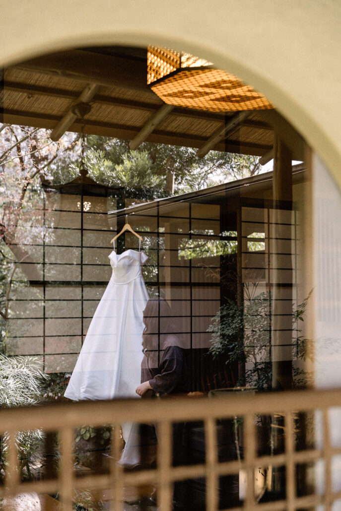 The wedding dress hangs in a window of the old inn, seen through a round arch past bamboo blinds, on the morning of a Jinya wedding.