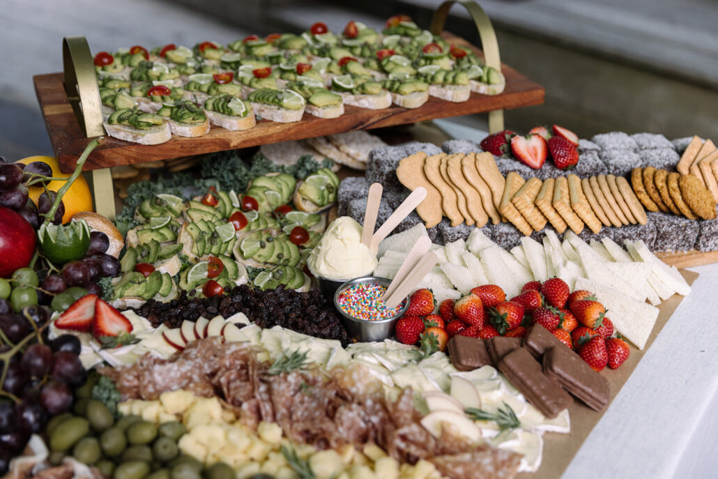 A grazing table at a wedding in Japan: avocado toasts on a tiered board, lamingtons, biscuits, strawberries, cheese, olives and salami.